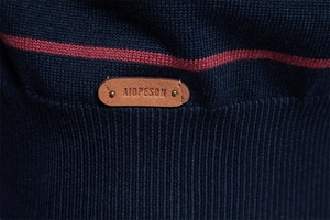 Detail of navy knit sweater featuring red stripe accents and brown leather brand patch