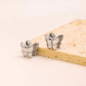 Polished silver butterfly earrings displayed on a beige textured stone block surface
