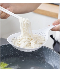 Close-up of white kitchen colander scooping noodles with chopsticks in home setting