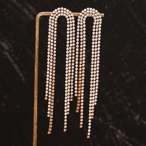 Close-up of gold-plated tassel earrings with micro-set rhinestones on a black background