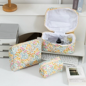 Three-piece floral quilted cotton makeup bag set on a clean white desk with accessories