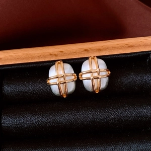 Macro detail of gold-plated square cross earrings with silk-luster white beads on velvet