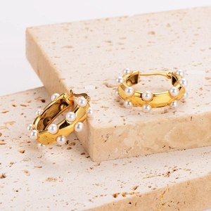 U-shaped hollow asymmetric 18k gold earrings with white pearls on stone background