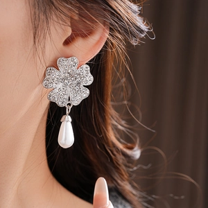 Detail view of silver clover earrings with sparkling rhinestones and white teardrop pearls