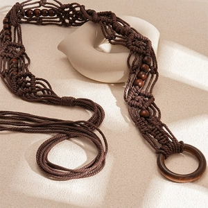 Close-up of bohemian brown braided cotton waist belt with wooden rings and beads on sand