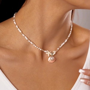 Macro detail of a beaded necklace featuring a pink shell, white starfish, and faux pearl