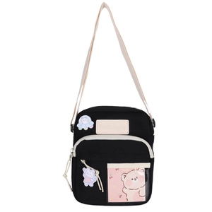 Détail du sac bandoulière en toile noire avec patchs de dessin animé et fente transparente