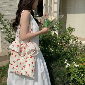 Close-up of a white canvas tote bag with red cherry prints and ruffled edge detailing