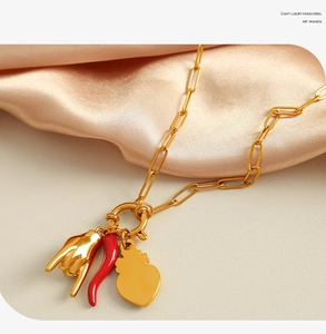 Detail of paperclip chain necklace with gold hand, heart, and red chili charms