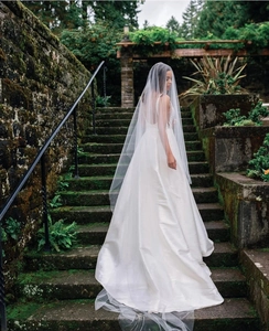 Detail of white long trailing bridal veil and backless satin wedding dress on stone steps