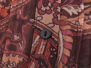 Close-up of bohemian paisley chiffon fabric texture and black button on a blouse