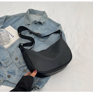 Flat lay of a black crescent crossbody bag with adjustable strap on a stylish white fabric