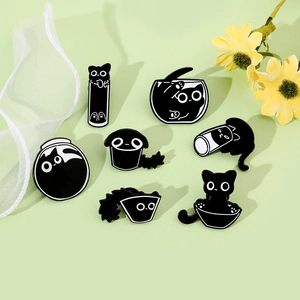 Flat lay of seven black cat enamel pins with floral accents on a green surface