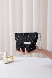 Polka dot travel cosmetic bag featuring a pearl handle strap and woven fabric texture