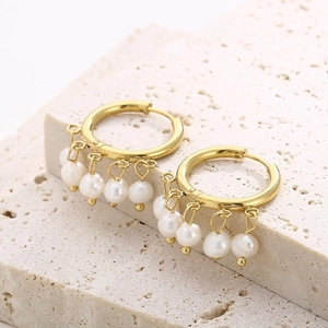 Macro shot of gold pearl hoop earrings on a textured stone, featuring luxury metal finish