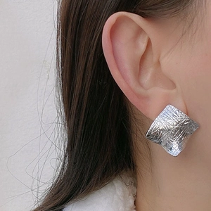 Detail of silver irregular square stud earring with textured metal surface on a model