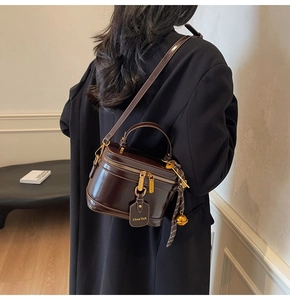 Detail of dark brown leather box bag with dual zippers and decorative checkered scarf