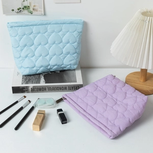 Quilted heart cosmetic bags in sky blue and lavender with zipper closure on desk