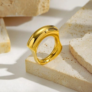 Detailed view of a gold irregular wave ring on a textured beige stone pedestal