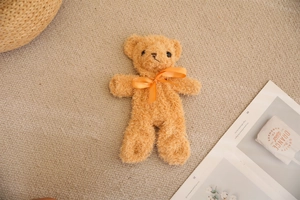 Detail of a light brown plush teddy bear with a bright orange satin bow on a textured rug