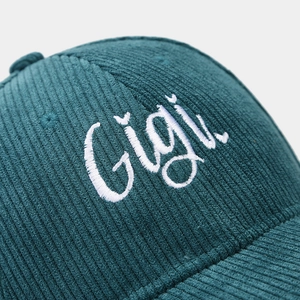 Detailed view of dark green corduroy fabric with white Gigi embroidery on baseball cap