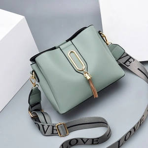 Mint green bucket bag with wide woven strap and tassel charm shown at a 45-degree angle