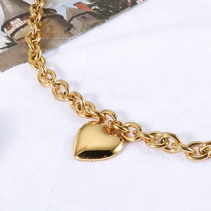 Close-up of golden stainless steel chain bracelet with a large heart pendant charm