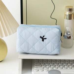 Close-up of light blue quilted cotton cosmetic bag with black bow embroidery on desk