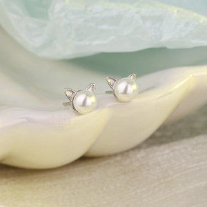 Macro view of minimalist cat-ear pearl stud earrings with a polished silver-tone finish