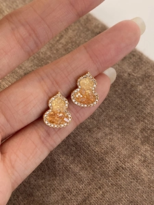 Macro shot of gold-plated gourd earrings with yellow gemstones and zircon pavé detail