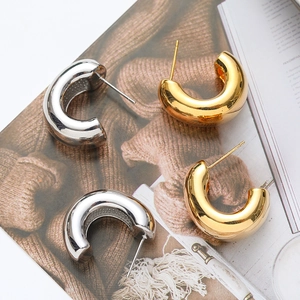 Polished C-shape thick hoop earrings in gold and silver finish on magazine background