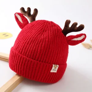 Close-up of red knit baby hat featuring plush reindeer antlers and a stitched baby label