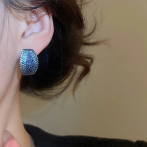 Detailed view of C-shaped blue crystal earrings worn by a model in soft lighting