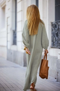 Dynamic back view of a woman walking in a loose bean green linen maxi shirt dress