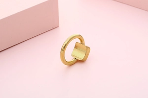 Detail of minimalist golden square ring featuring a concave geometric top on a pink base