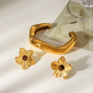 Detail of gold-plated wavy cuff bracelet and leopard floral stud earrings on a white background