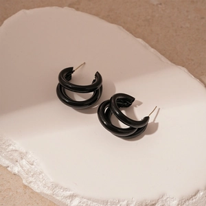 Vue détaillée de boucles d'oreilles noires en forme de C sur un socle en pierre
