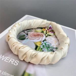 Detailed close-up of a pleated cream satin headband with elegant scrunchie texture