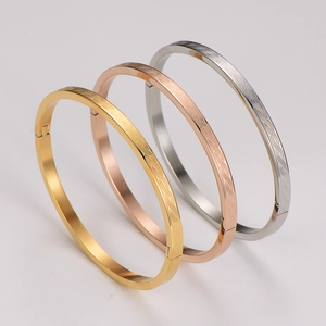 Close-up of tricolor stainless steel bangles with etched wave pattern and side hinge closure