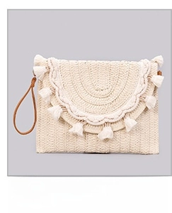 Close-up of woven straw clutch bag featuring fringe tassel details and a leather wrist strap