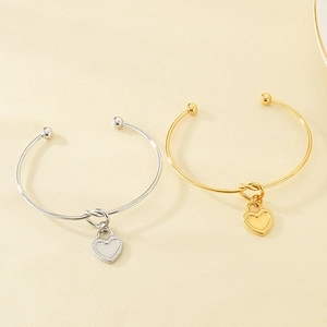 Detailed view of polished gold and silver heart lock knot bracelets on cream paper