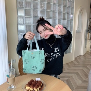 Detail of mint green corduroy tote bag with black smiley face print in cozy cafe setting