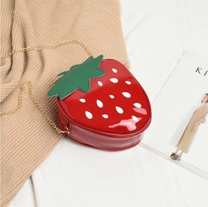 Detail of red strawberry crossbody bag with green leaf flap and gold chain strap