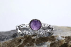 Detailed view of silver stackable rings with round purple gemstone on textured rock