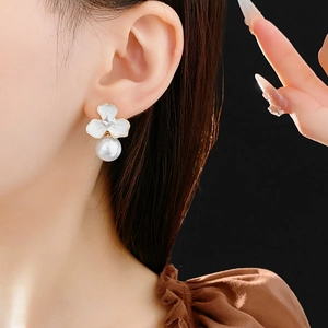 Close-up of elegant gold flower earring with crystal center and a hanging white pearl