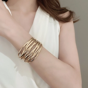 Close-up of a layered golden metal cuff bracelet worn on a wrist for a minimalist style