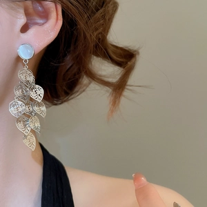 Close-up of silver leaf-shaped tassel earrings with opal detailing on a female model