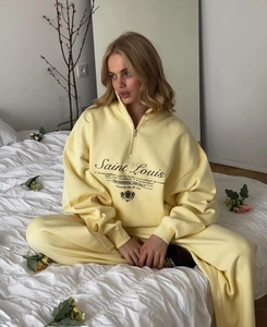 Detail of pale yellow fleece tracksuit featuring embroidered logo and half-zip sweatshirt