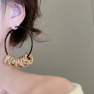 Detail view of a model wearing large black leather cord hoops with gold and silver beads