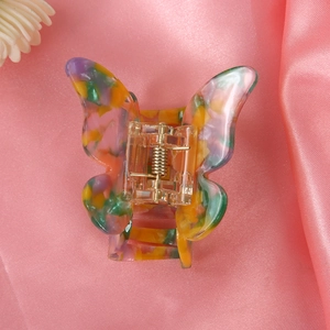 Detailed top view of butterfly hair claw clip with colorful mosaic pattern on pink satin